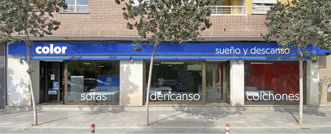 Fachada de Color sueño y descanso en la calle Jerónimo Santa Fe de Lorca, con el toldo azul y los rótulos de sofás y colchones